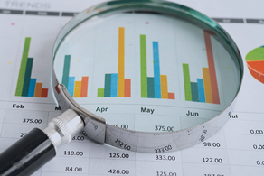 Image of a magnifying glass laying over a paper monthly expense report with charts.