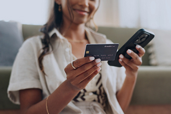 Image of a young woman holding her cell phone in one hand and her credit card in another.